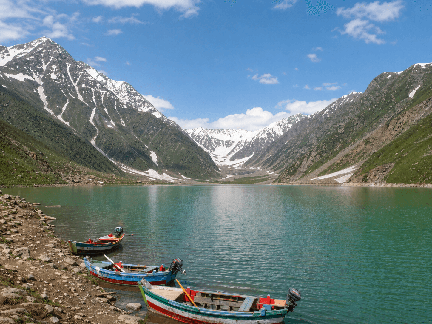 Colorful wooden boats on Lake Saif-ul-Muluk beneath the snow-streaked peaks near Naran