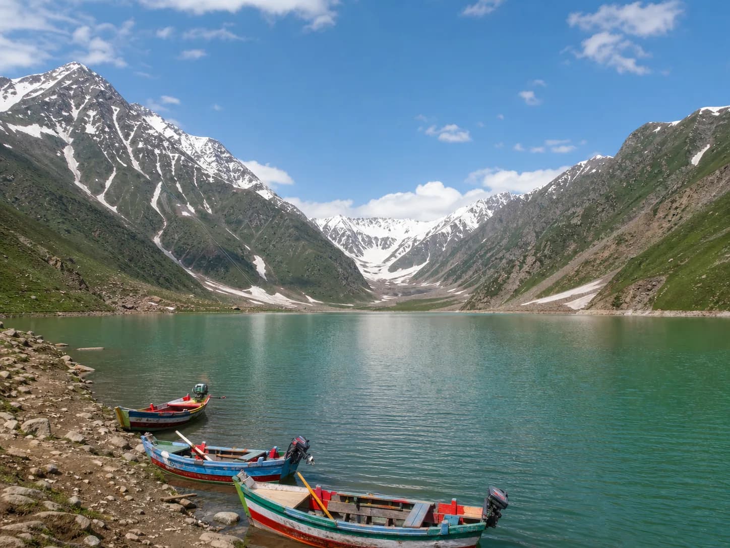 Colorful wooden boats on Lake Saif-ul-Muluk beneath the snow-streaked peaks near Naran