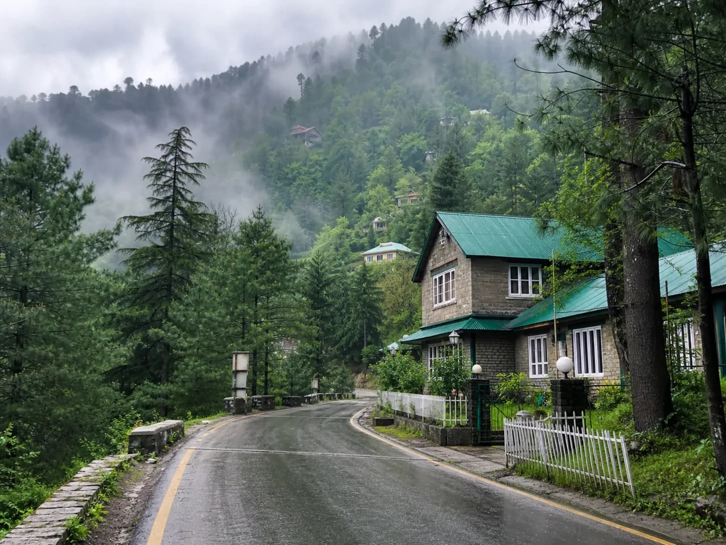 A colonial stone cottage and winding road among misty pine forests in Nathia Gali